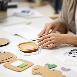 Packaging designer at a desk comparing eco-friendly container finishes and die-cut samples